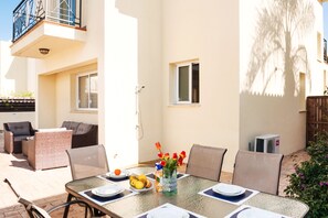 A sunlit patio with a dining table set for two, surrounded by wicker furniture and a small garden. - Natalie Villa CL 41 (Paralimni)