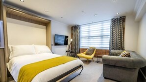 Quarto de hotel com cama, sofá, poltrona e televisão.