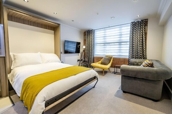 A hotel room with a bed, a sofa, a chair, and a TV.