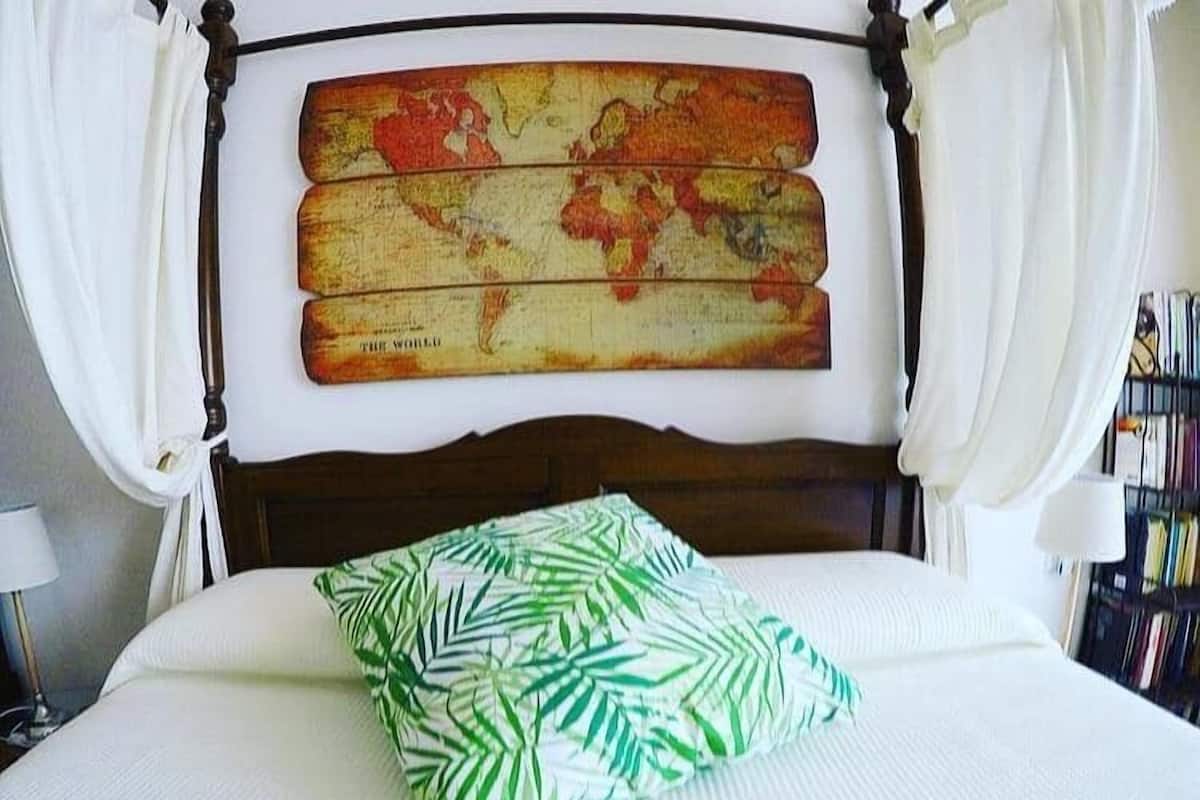 Un lit avec une tête de lit ornée d’une carte du monde, une literie blanche et un coussin à motifs de feuilles vertes.