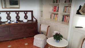 A cozy reading nook with a wooden bench, a small round table with a potted plant, and a bookshelf filled with books. - La Terrazza di Anna (Sassari)