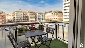 Un balcón con mesa y sillas, un pequeño jardín con flores y vistas de edificios circundantes.