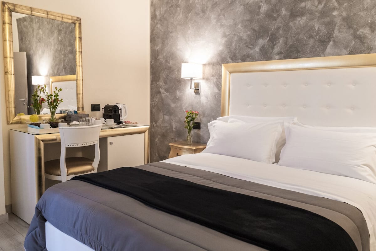 A hotel room with a bed, a desk, a chair, a lamp, and a mirror.