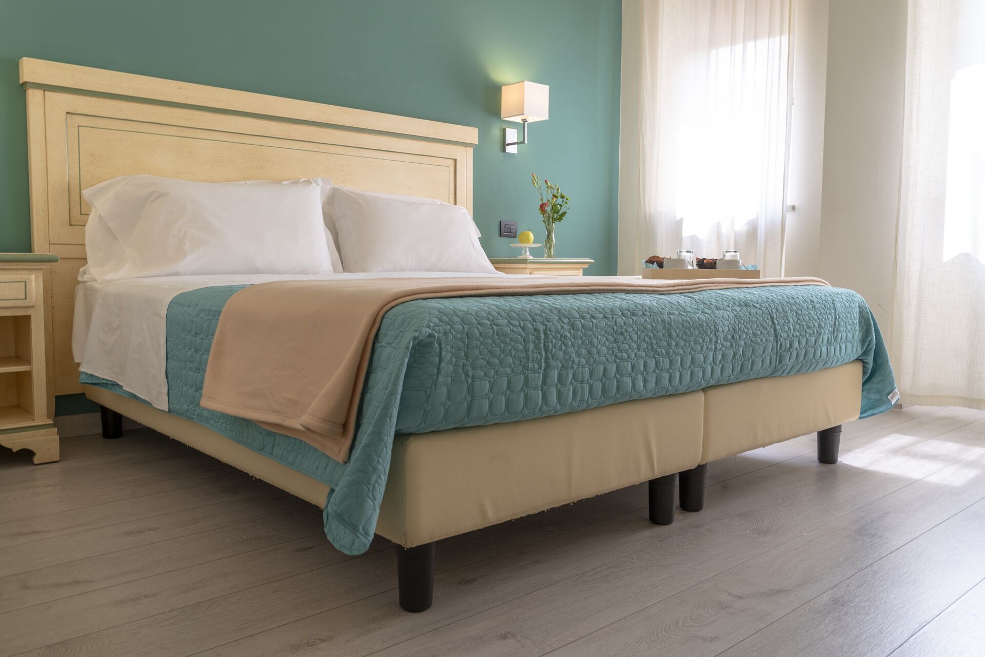 Una cama bien hecha con un cabecero color beige, una colcha acolchada color verde azulado y dos almohadas blancas.