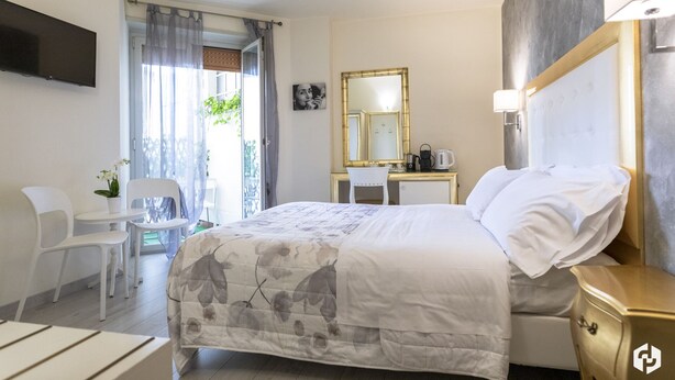 Habitación de hotel con cama, escritorio, silla, televisor y baño visible a través de una puerta de cristal.