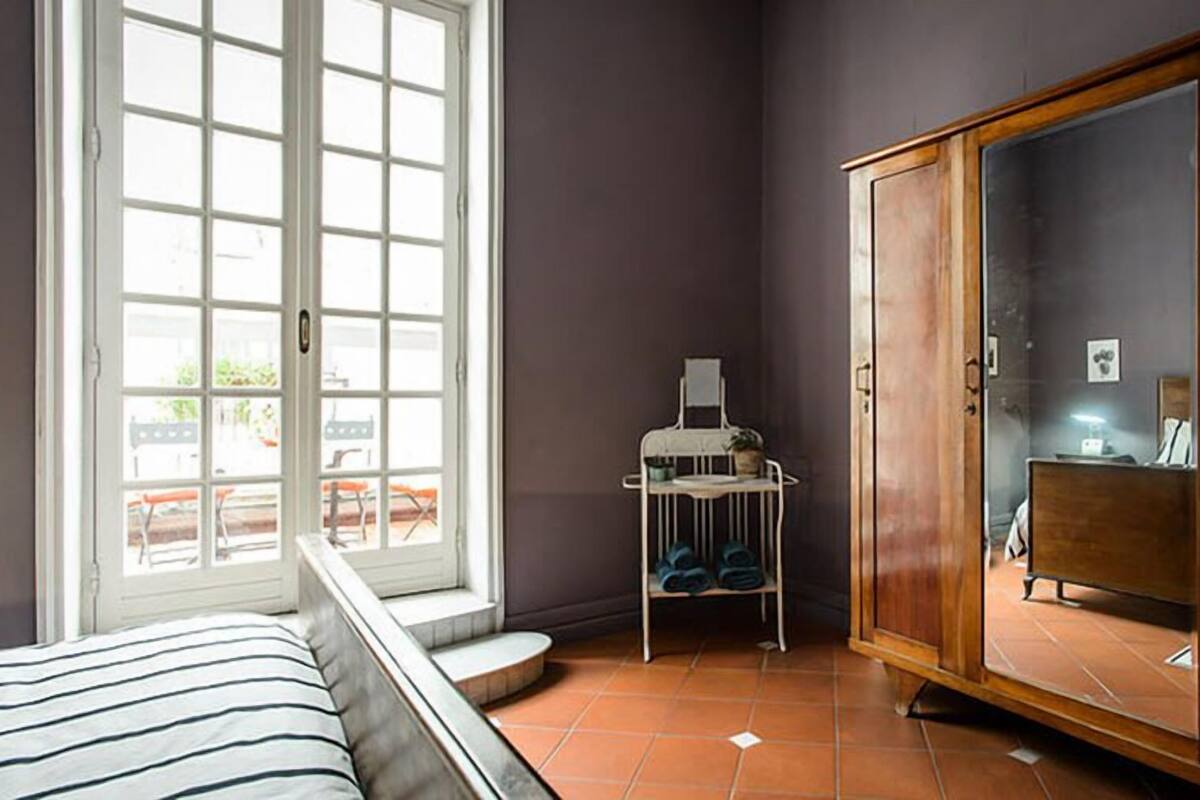 Un dormitorio con cama, armario, ventana y una mesita de noche con lámpara.
