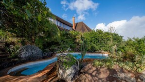 A pool surrounded by rocks and lush greenery, with a building in the background. - Pumzika Tu (Kwale)