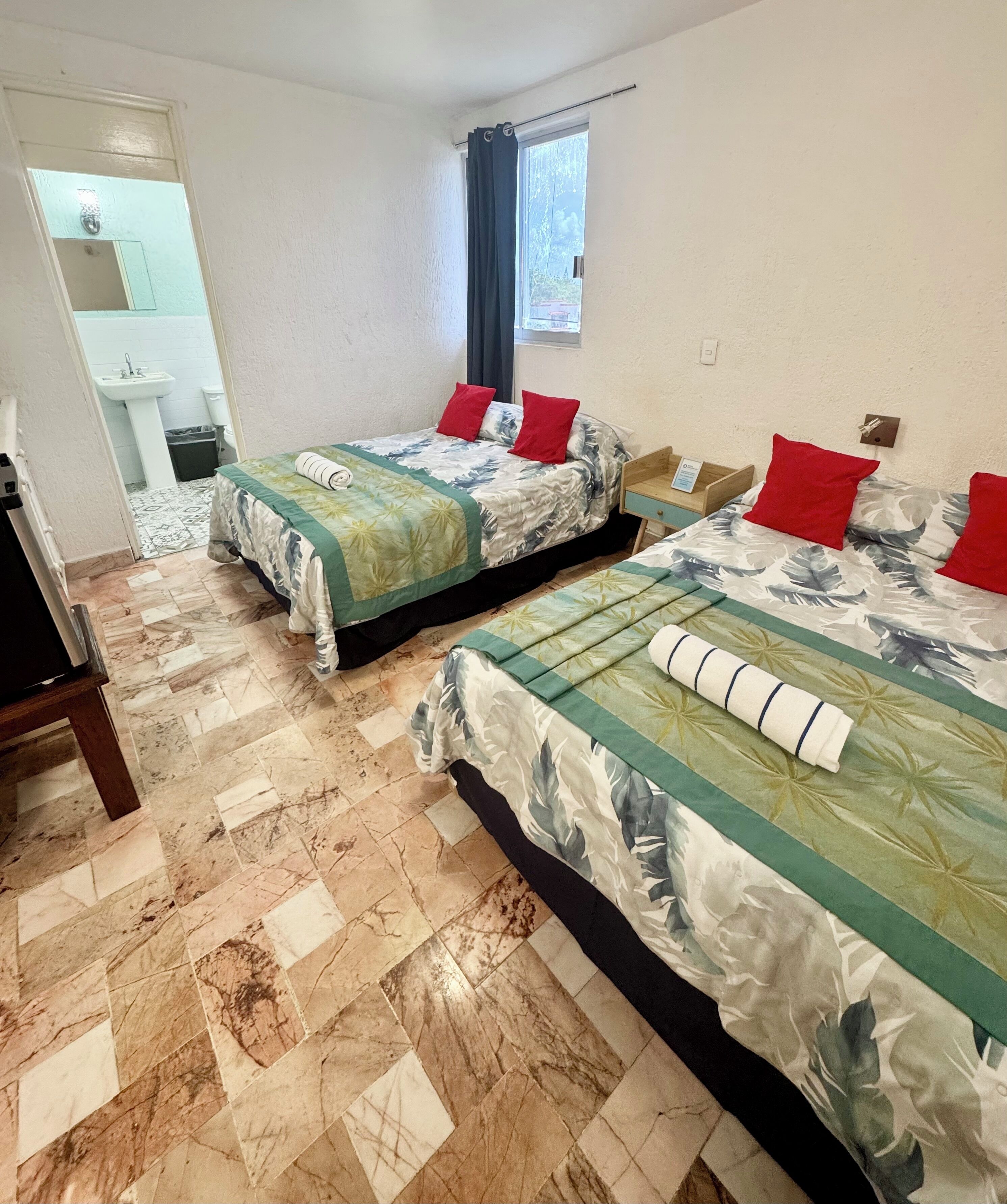 Une chambre d’hôtel avec deux lits, une salle de bain et une fenêtre avec des rideaux.