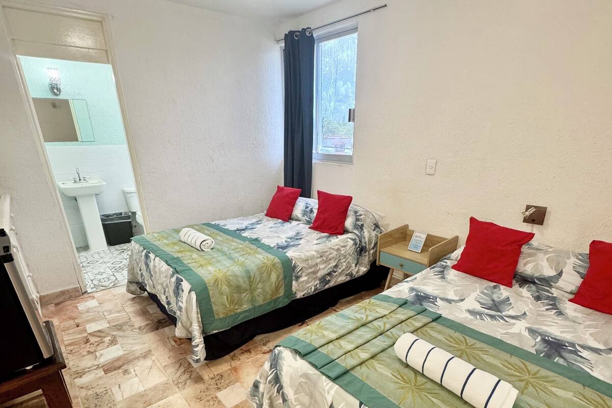 A hotel room with two beds, a bathroom, and a window with curtains.