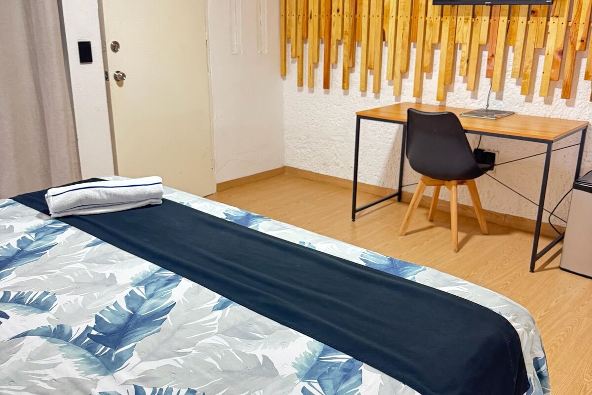 Camera d'albergo con un letto, una scrivania, una sedia e un televisore montato su una parete in legno.