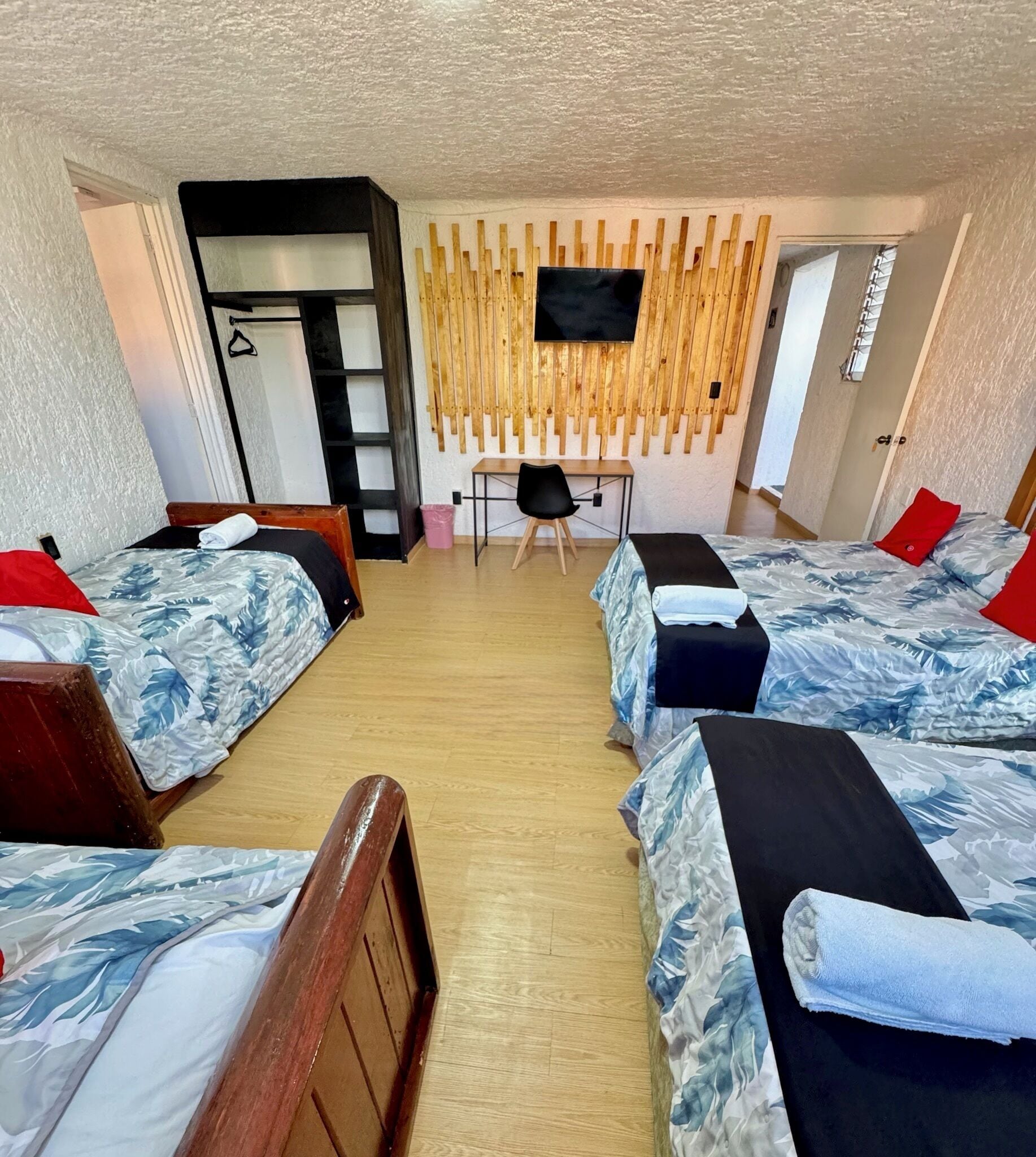 Une chambre d’hôtel avec quatre lits, un bureau et un téléviseur fixé au mur.