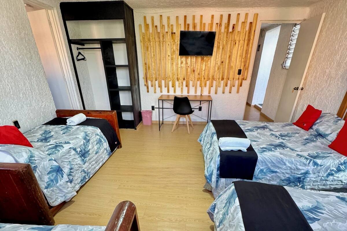 A hotel room with four beds, a desk, and a TV mounted on the wall.