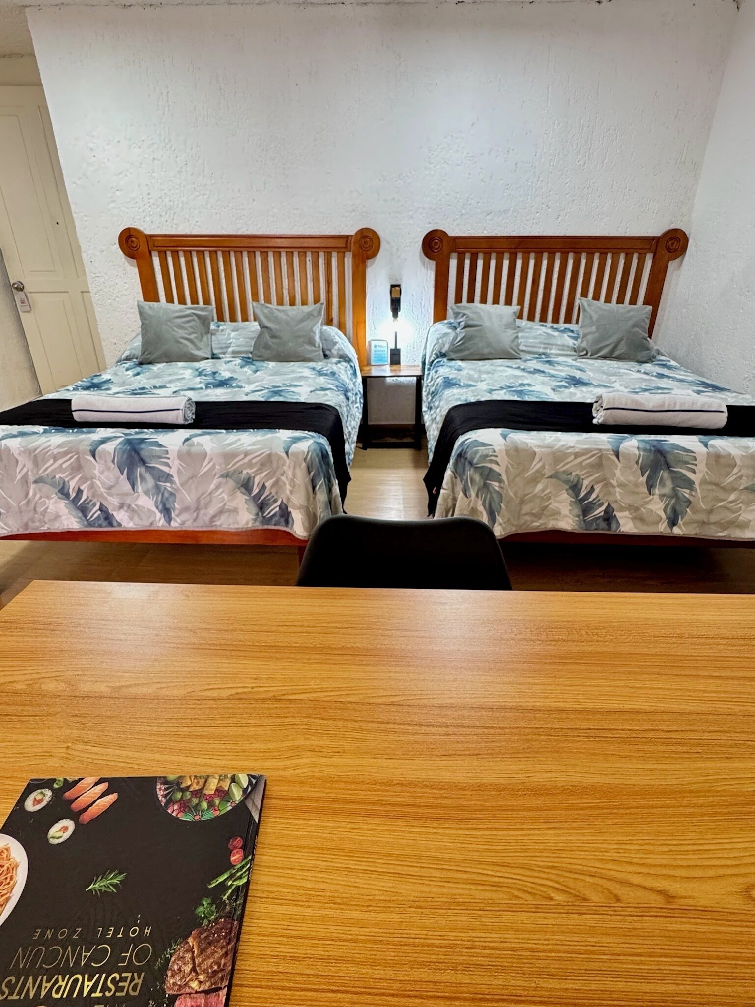 Une chambre d’hôtel avec deux lits simples, une table en bois et un livre posé sur la table.