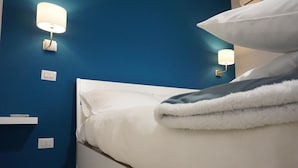 Un dormitorio con cama blanca, paredes azules y dos lámparas fijadas a la pared.