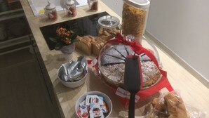 Una mesa de buffet con distintos alimentos, incluyendo un pastel, pan y aperitivos envasados.