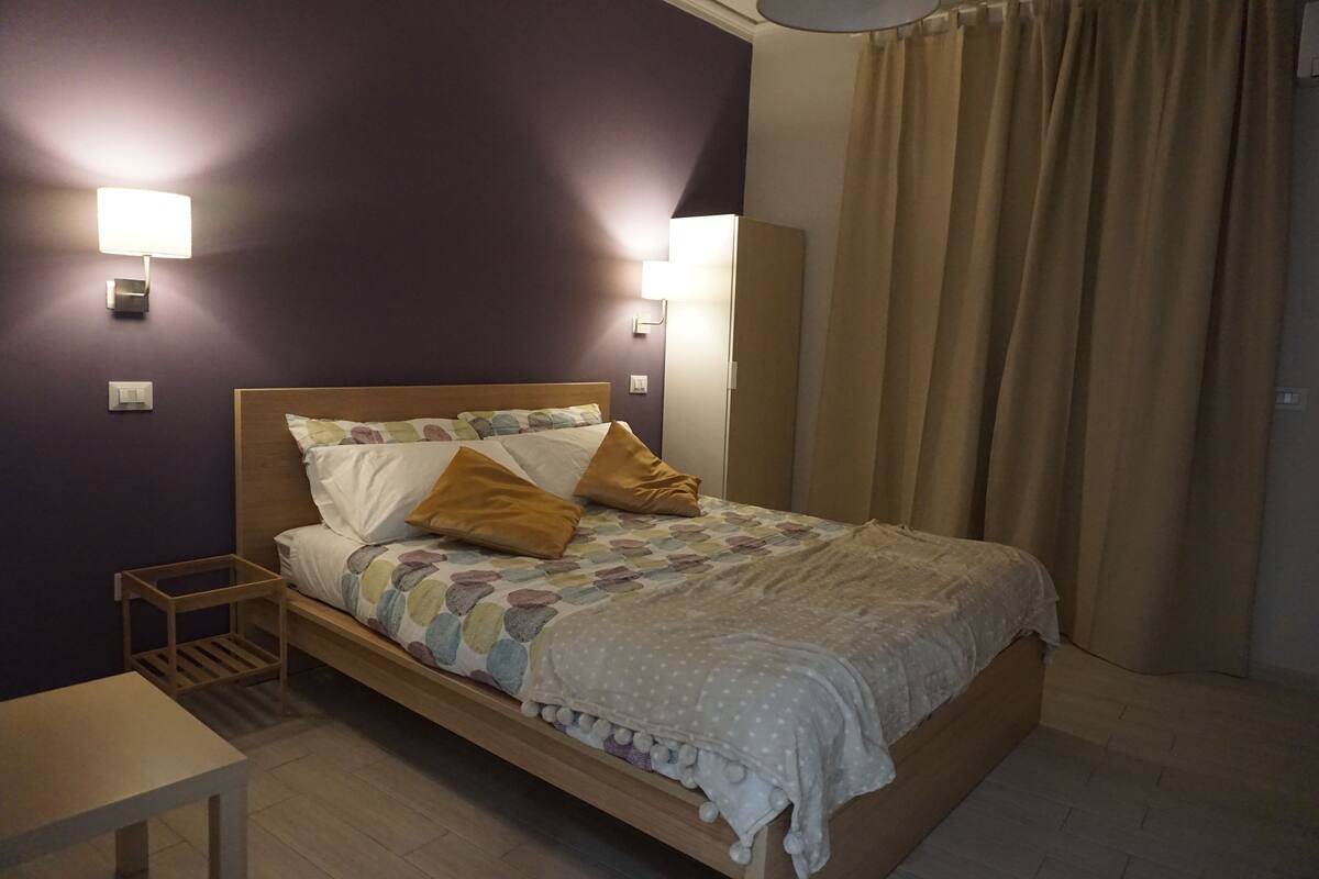 A neatly made bed with a patterned bedspread and two pillows, a bedside table, and two wall-mounted lamps.