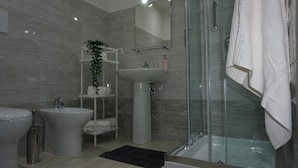 Un baño moderno con ducha envuelta en vidrio, lavamanos sobre pedestal y bidé.