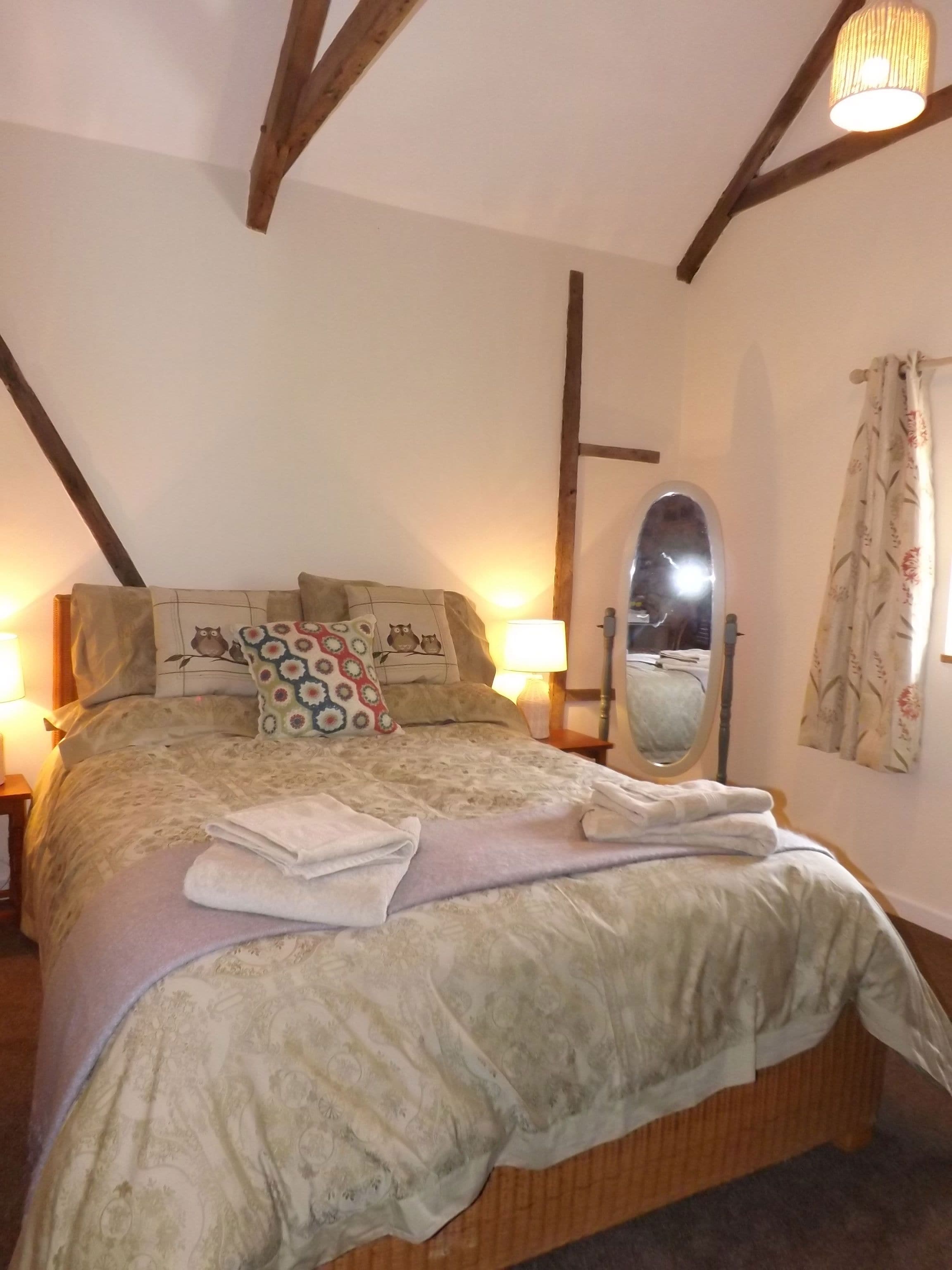 Un dormitorio con cama, almohadas, un espejo y una ventana con cortinas.