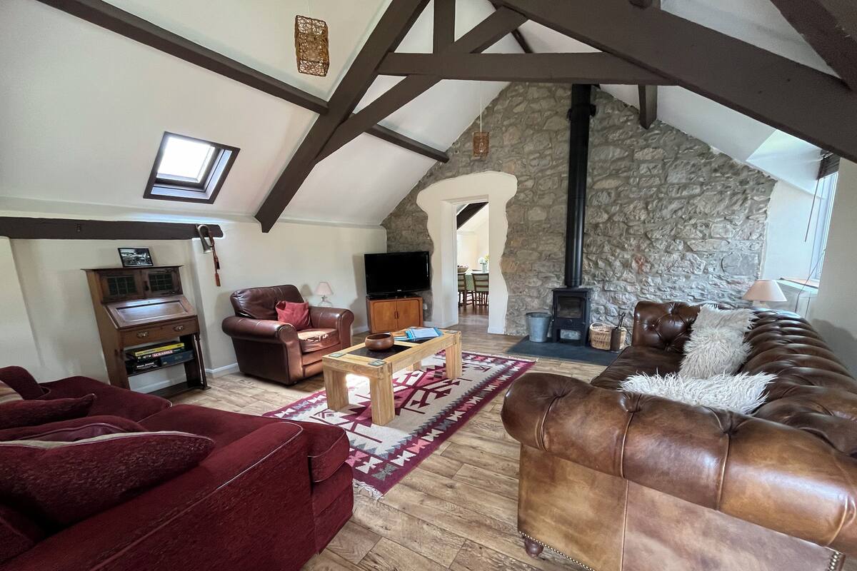 A spacious living room with a stone wall, wooden beams, a fireplace, leather sofas, and a television.