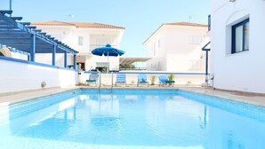 A swimming pool with blue tiles, surrounded by white buildings with balconies and blue railings. - Sirina Villa STN 29 (Paralimni)