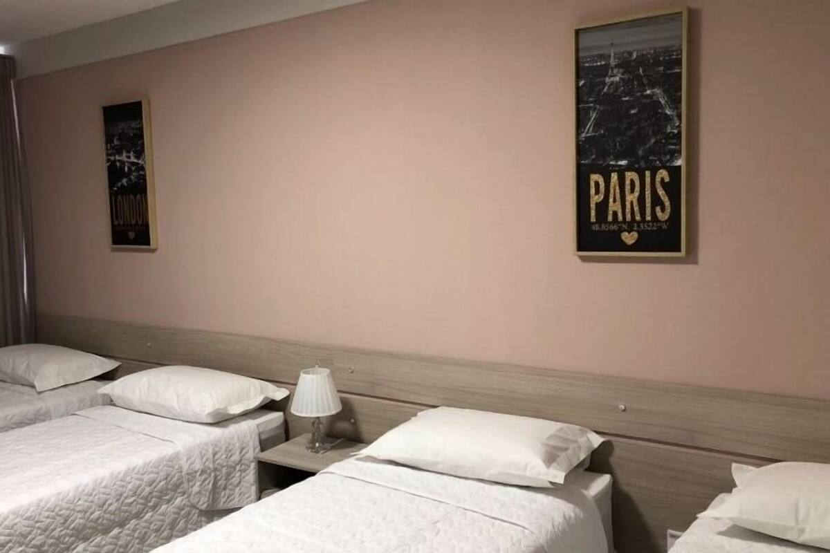 Habitación de hotel con dos camas individuales, una mesita de noche con lámpara y dos carteles en la pared.