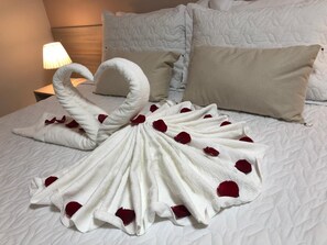 A neatly made bed with a towel arranged in the shape of a swan, adorned with rose petals, and a lamp on the bedside table. - Hotel San Remo (Jequie)