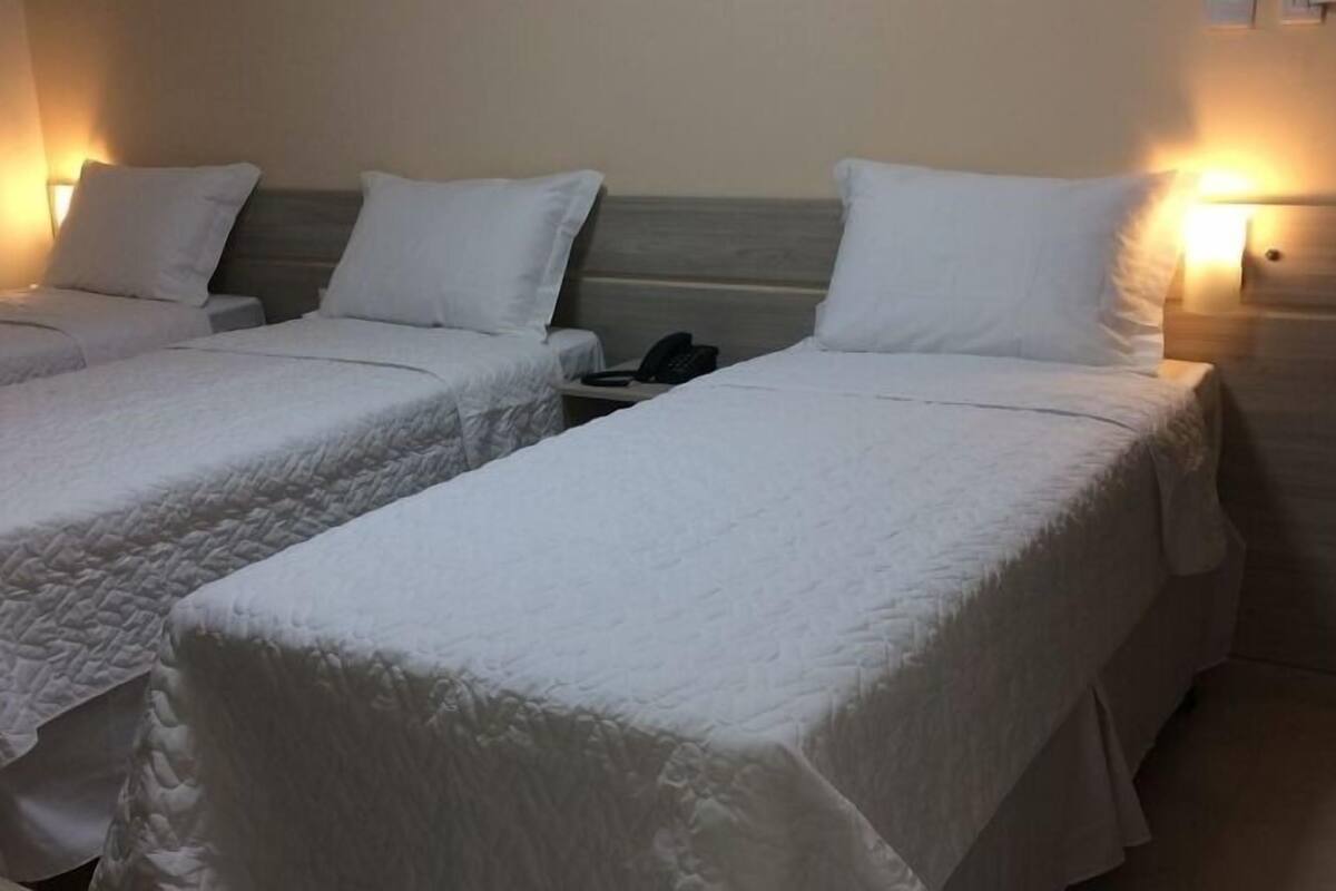 Dos camas individuales con sábanas blancas, una mesita de noche con teléfono y una lámpara de pared.