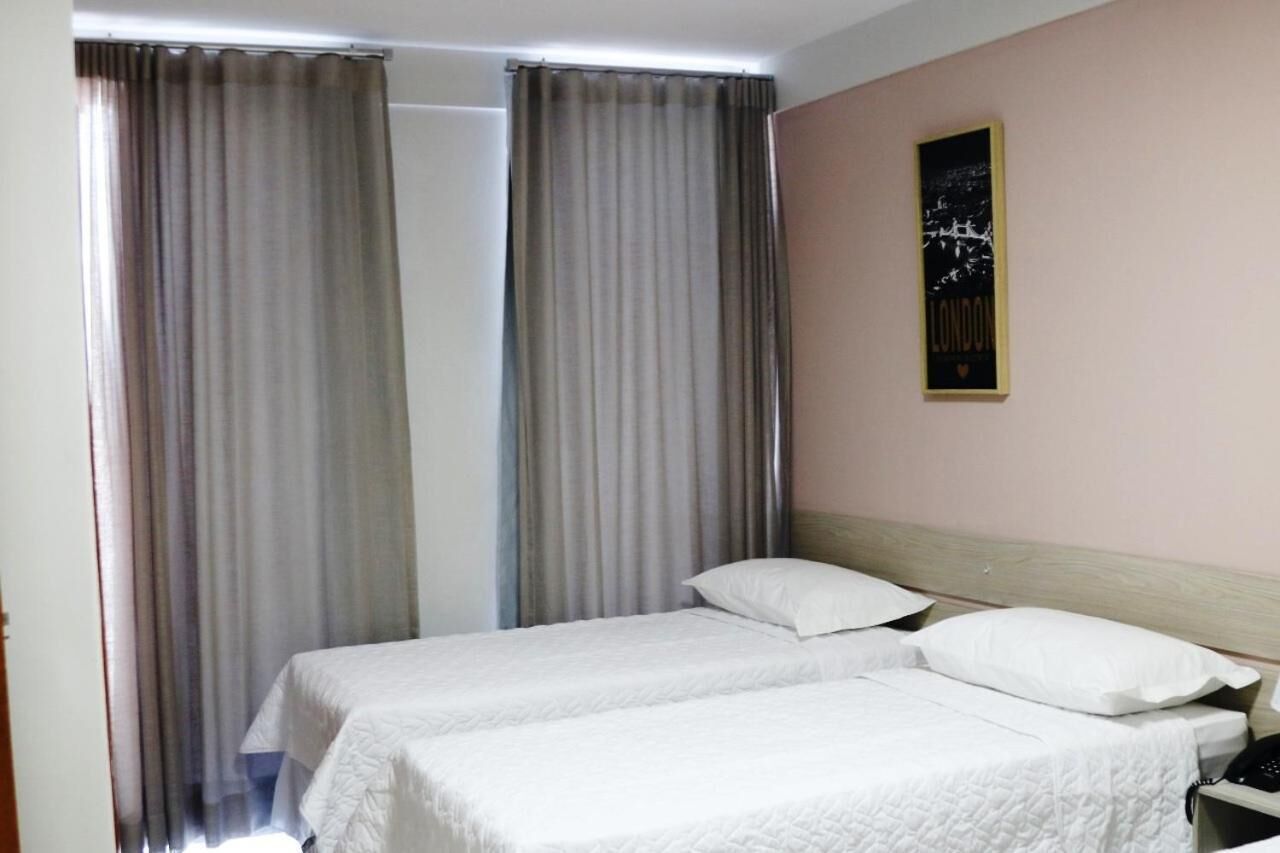 A hotel room with two single beds, a wooden headboard, a nightstand, and a framed picture on the wall.