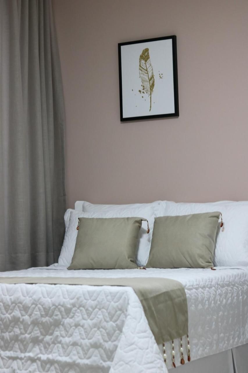 A bed with white bedding and two green pillows, a framed artwork on the wall, and a grey curtain.