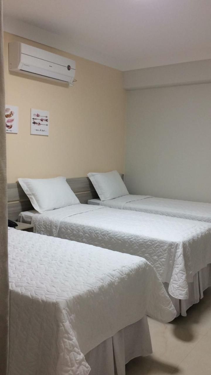 A room with two single beds, a wall-mounted air conditioner, and two framed pictures.