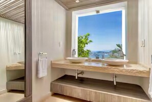 Ein Badezimmer mit zwei Waschbecken, einem großen Fenster mit Meerblick und einem Handtuchhalter.
