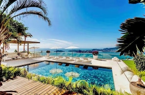 Ein Poolbereich mit klarem, blauem Wasser, Liegestühlen und Blick auf den Ozean.
