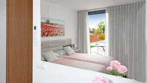 A modern bedroom with a large bed, a nightstand, a wall-mounted control panel, and a view of a garden through a sliding door. - COZY HOLIDAY VILLA IN THE HEART OF MALLORCA (Sa Pobla)