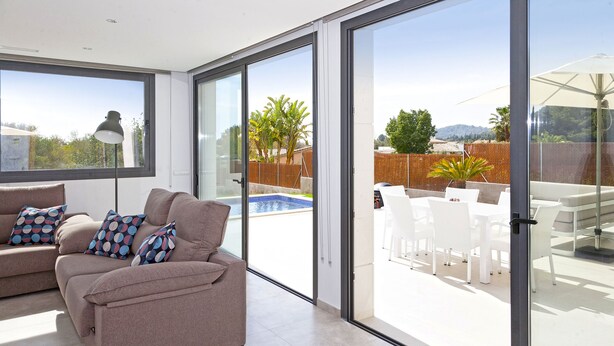 A modern living room with a sofa and chairs, large sliding glass doors leading to an outdoor patio with a pool and white furniture. - COZY HOLIDAY VILLA IN THE HEART OF MALLORCA (Sa Pobla)