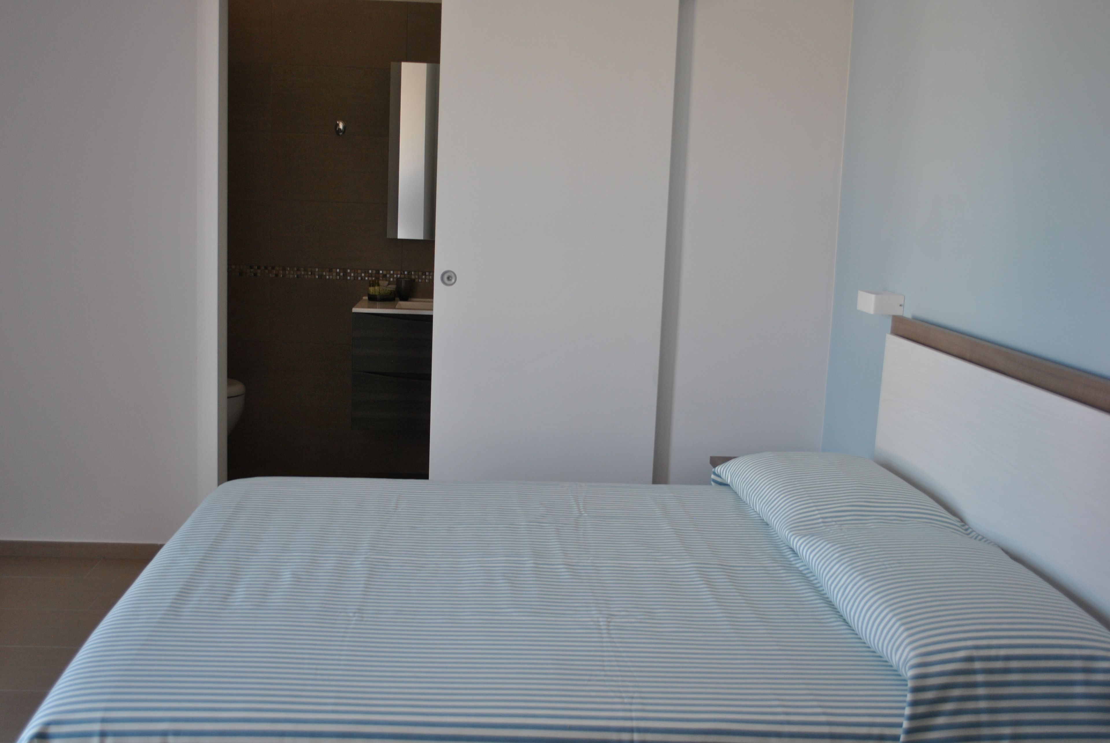 Un dormitorio con una cama, una puerta que da a un baño y un espejo fijado a la pared.