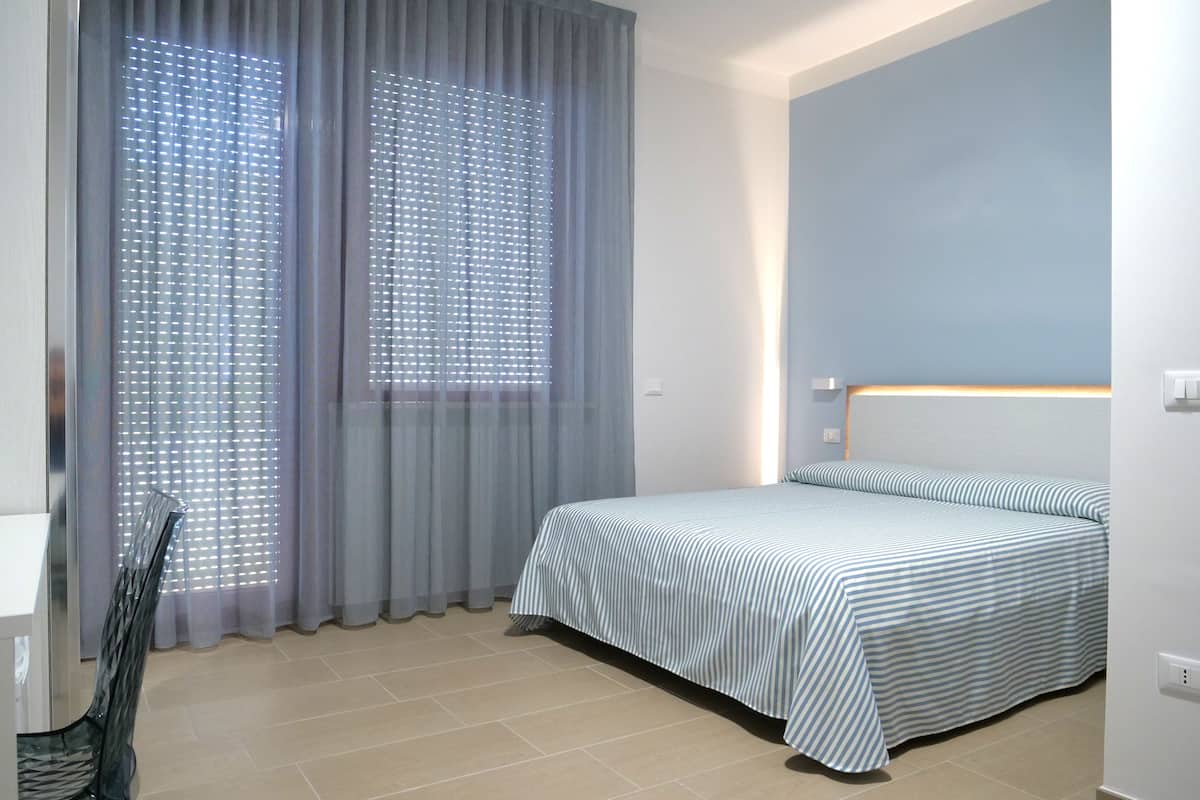 Ein Schlafzimmer mit Bett, Vorhängen, einem Sessel und einem Nachttisch.