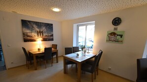 En matplats med ett träbord och stolar, en målning av en bro, en klocka och ett fönster som släpper in naturligt ljus.