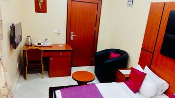 Una habitación de hotel con cama, escritorio, silla, una mesita y un armario.