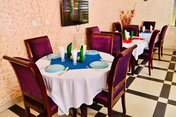 Un comedor con mesas redondas, sillas moradas y manteles blancos.