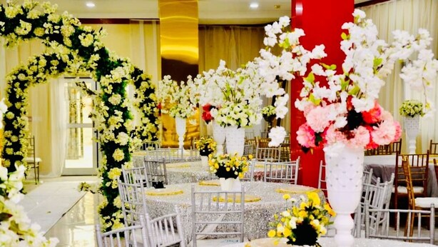 Un salón de banquetes con mesas redondas, sillas blancas y centros de mesa florales.