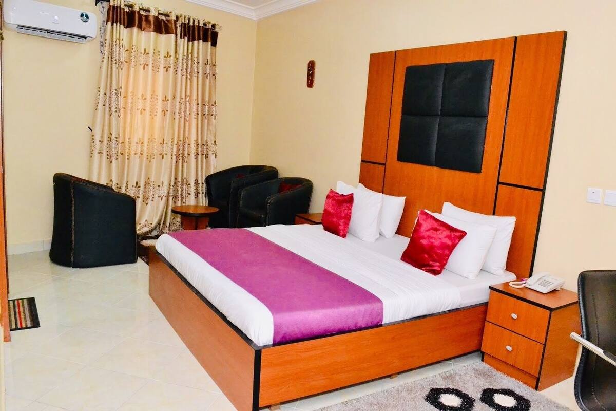 A hotel room with a wooden bed, a desk, a chair, and a small table.