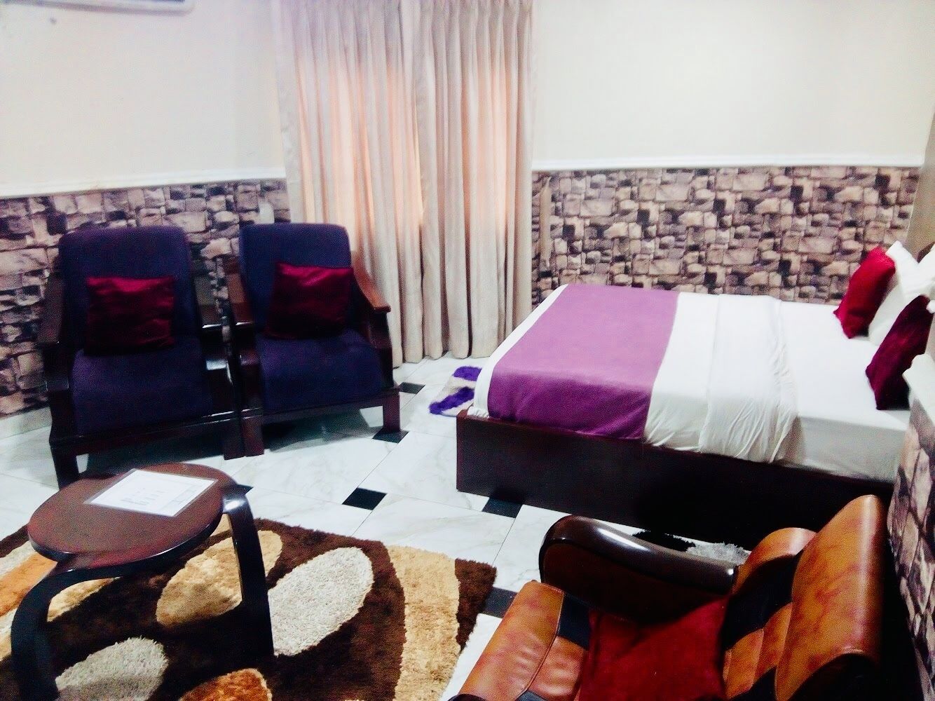 A hotel room with a bed, two armchairs, a small table, and a patterned rug.