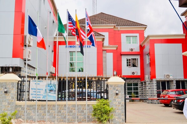 A building with multiple flags, a sign for a pool party, and a gated entrance. - Limoh Suites (Benin City)