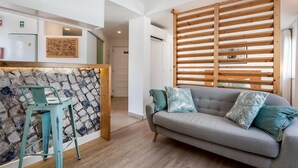 A modern living room with a grey sofa, teal cushions, a stone wall, and a wooden slatted partition.