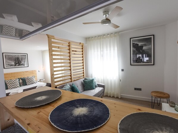 A modern living room with a wooden dining table, a sofa, and a ceiling fan.