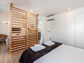 A modern hotel room with a wooden partition, a bed with white linens, a wardrobe, and an air conditioning unit.