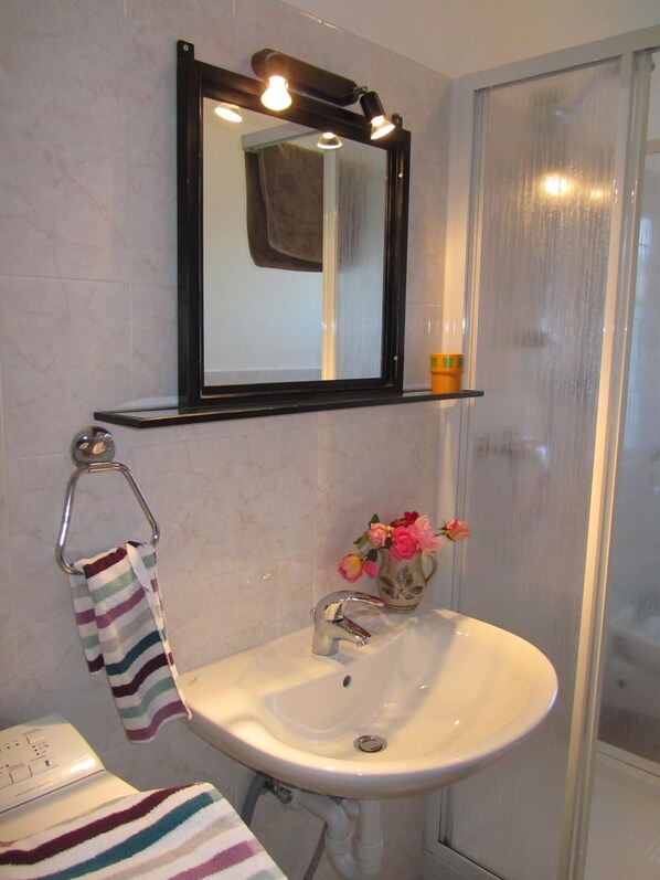 A bathroom with a white sink, a striped towel, a mirror, and a vase with flowers.