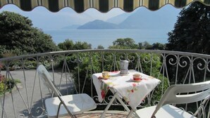 A balcony with a table set for two, overlooking a scenic view of a lake and mountains. - Situated in a beautiful & relaxing place on Lake Como,. Perfect family of 4. (Musso)