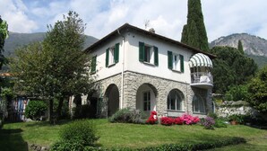 A white building with green shutters, stone arches, and a balcony with a striped awning. - Situated in a beautiful & relaxing place on Lake Como,. Perfect family of 4. (Musso)
