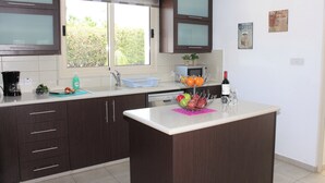 Una cocina con armarios de madera oscura, una ventana con vistas a la vegetación, un lavamanos y una encimera con un frutero y una botella de vino.